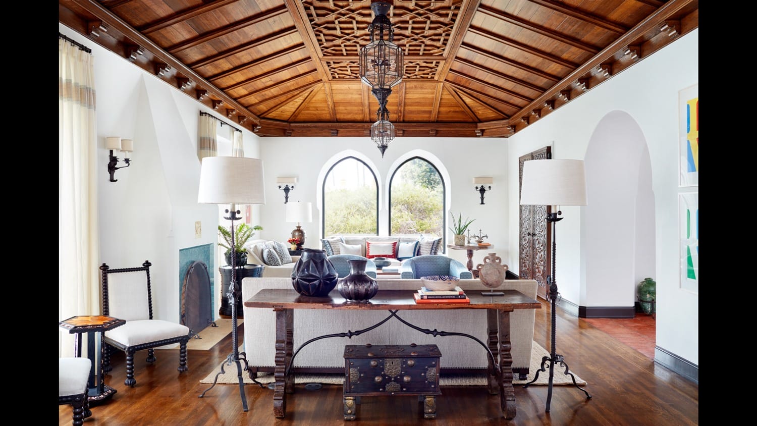 Spacious living room with wooden ceiling, large windows, elegant furniture, and decorative lamps.