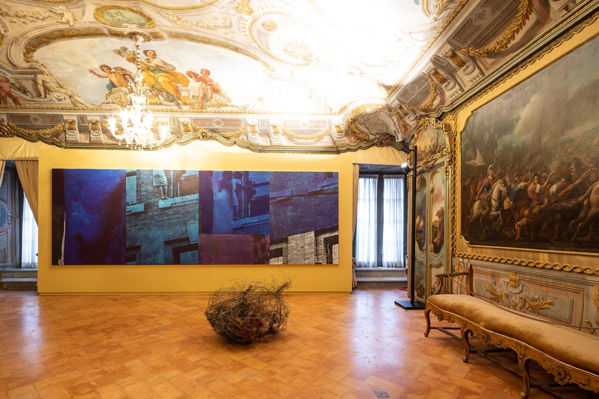 Ornate gallery room with chandelier, ceiling mural, modern art displayed on wall, and historical painting on right.