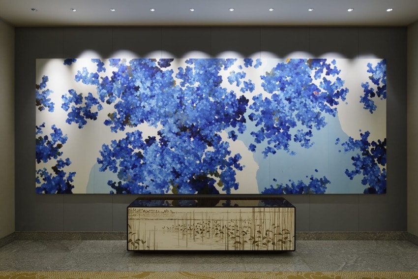 Abstract blue and white wall art with floral patterns above a decorative sideboard in a modern gallery or hotel setting.