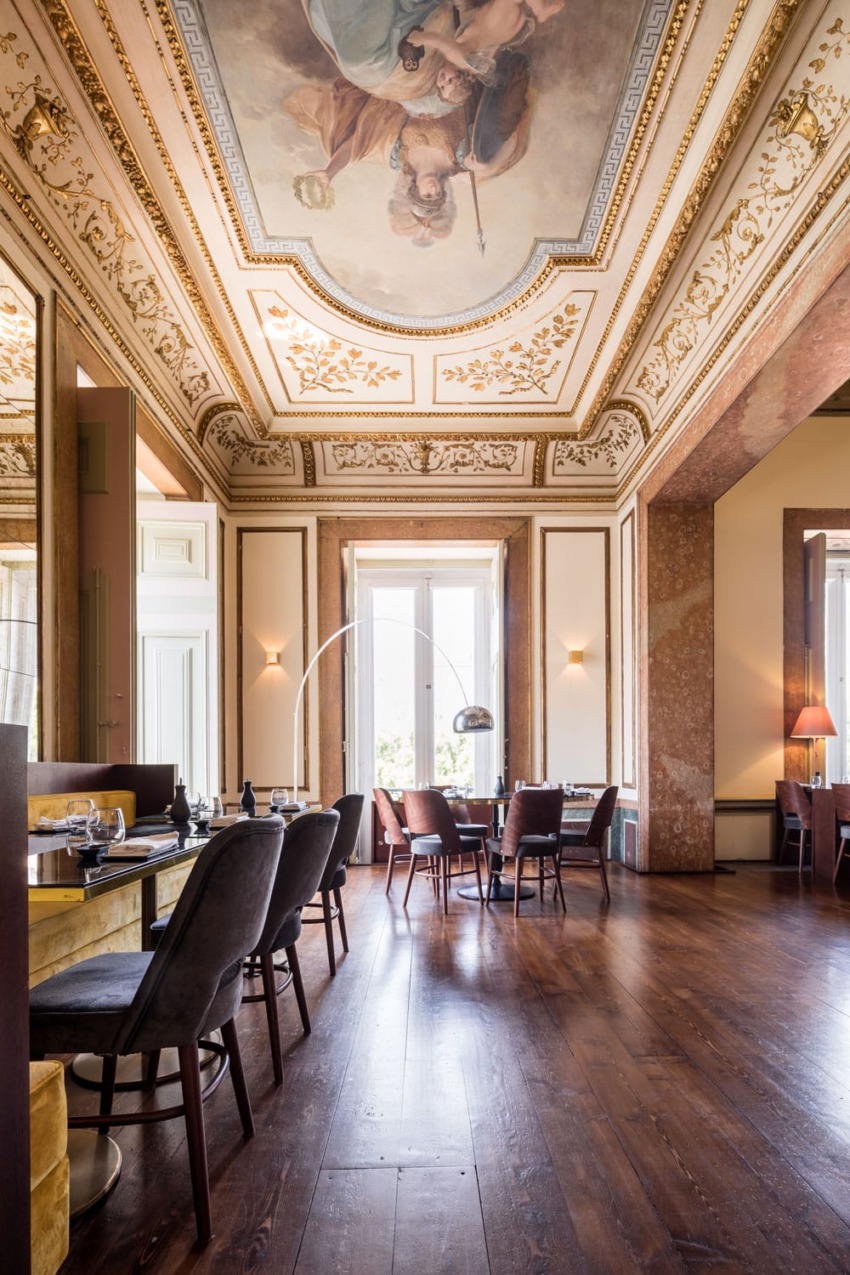 Elegant dining room with high ornate ceiling, large windows, wooden floor, and modern furniture.