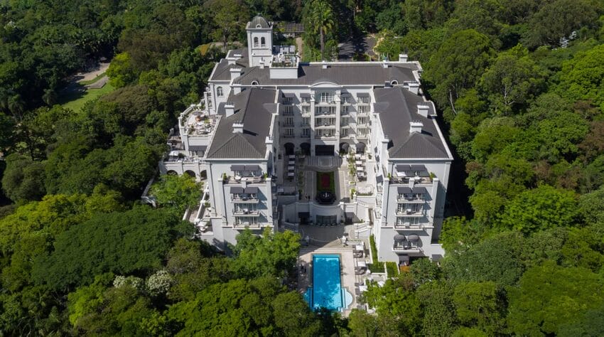 Aerial view of a luxurious hotel surrounded by lush greenery, featuring a central pool and elegant architecture.