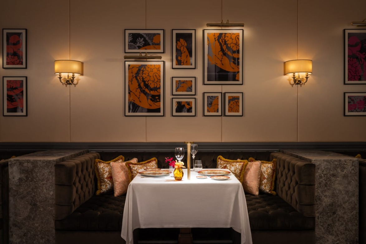 Elegant restaurant booth with a white tablecloth, dinnerware, wine glasses, and art-adorned walls in warm lighting.