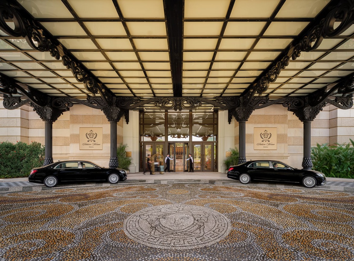 Luxury hotel entrance with sleek black cars, ornate ironwork, and a mosaic stone driveway, showcasing elegance and grandeur.