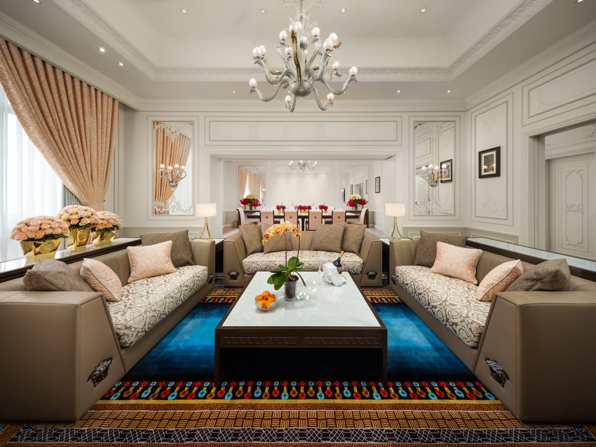 Luxurious living room with elegant chandeliers, plush sofas, coffee table, and decorative accents in an opulent setting.