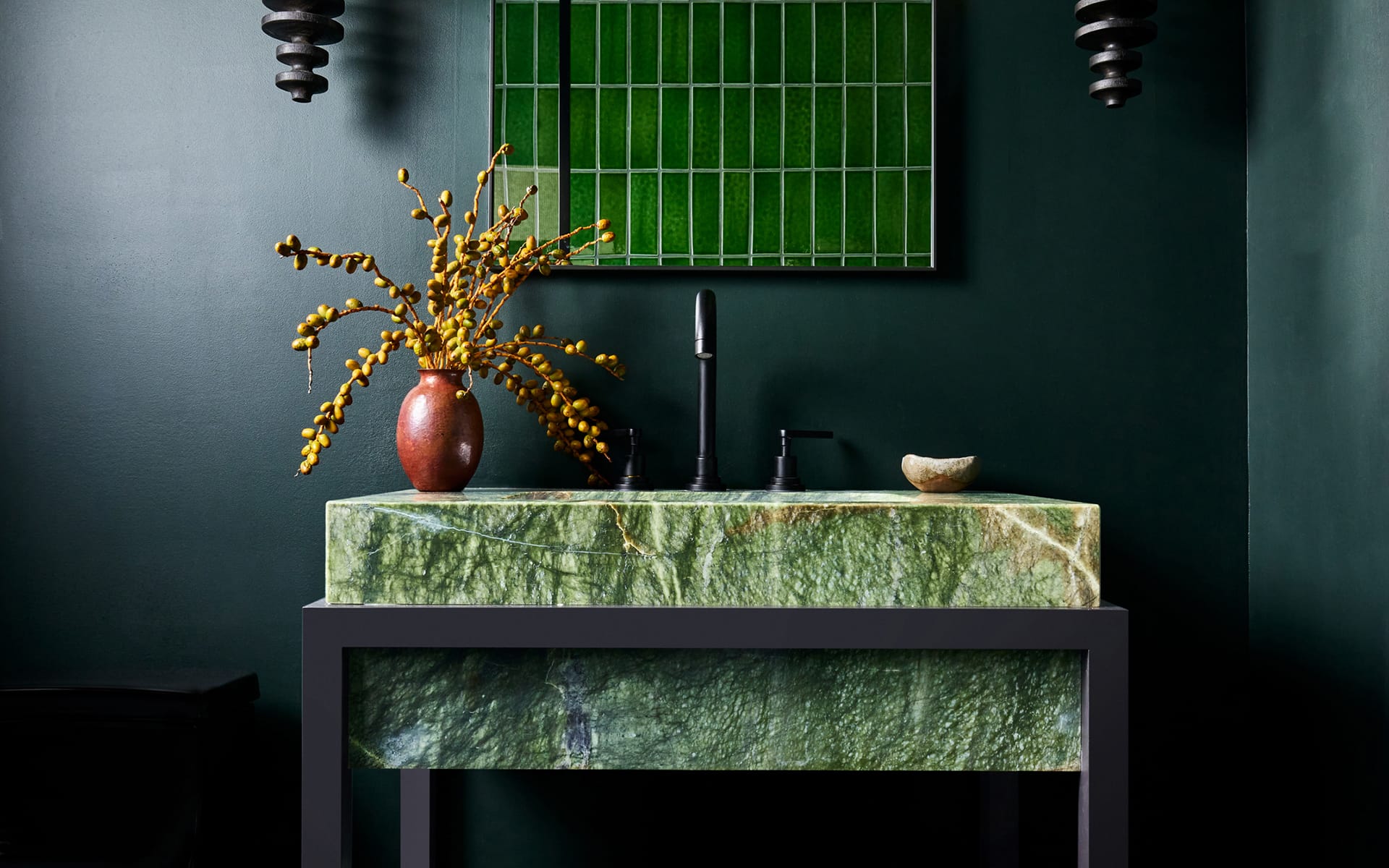 Modern green stone sink with black faucet, yellow flowers in vase, and geometric wall art in dark green bathroom.