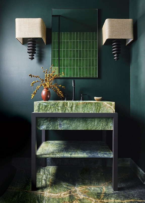 Modern bathroom with green marble sink, rectangular mirror, and wall-mounted light fixtures on dark green walls.