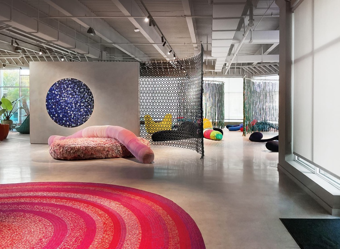 Modern art gallery with colorful abstract sculptures, circular art piece on wall, and vibrant patterned rug.