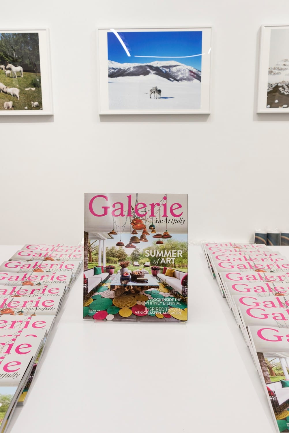 Magazine titled "Galerie" on a table in an art gallery with landscape photos on the walls in the background.