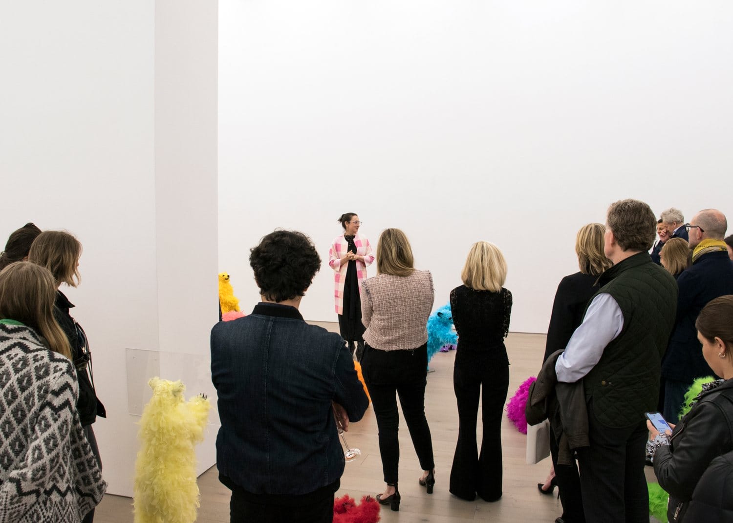 A person speaking to an audience in a gallery surrounded by colorful feather sculptures.