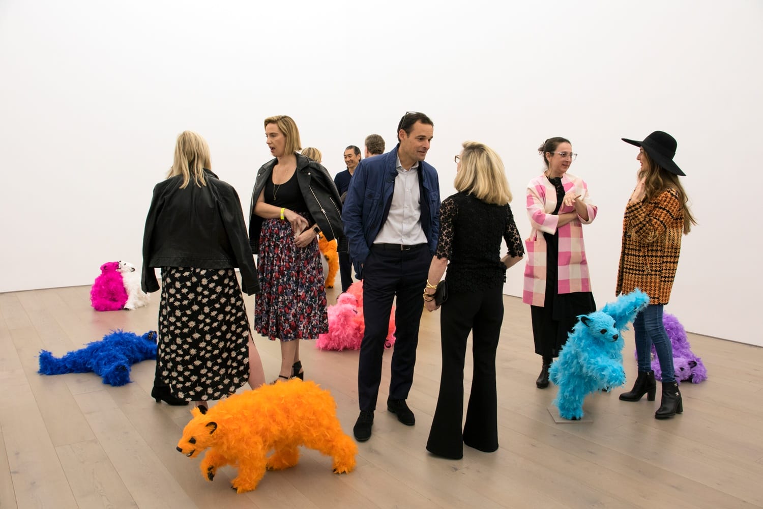 People interacting with colorful, fluffy animal sculptures in an art gallery with white walls and wooden flooring.