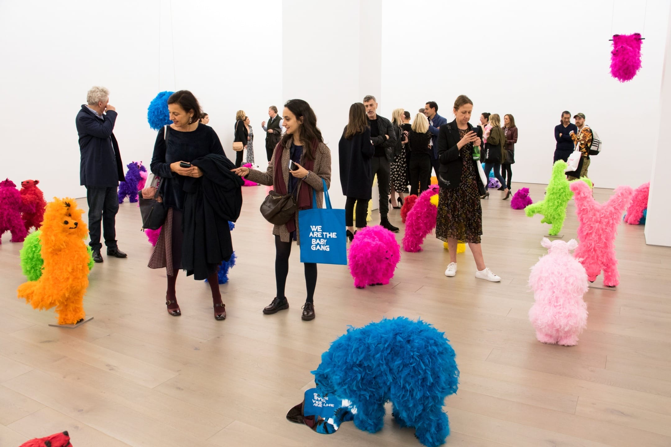 People interacting with colorful, fuzzy sculptures at an art exhibit in a modern gallery space.