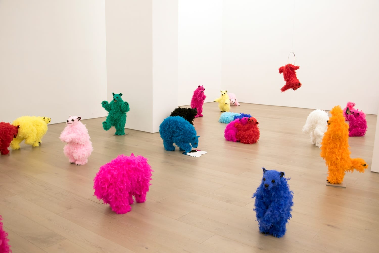 Colorful, fluffy animal sculptures in an art gallery, standing and hanging in a minimalistic white space.