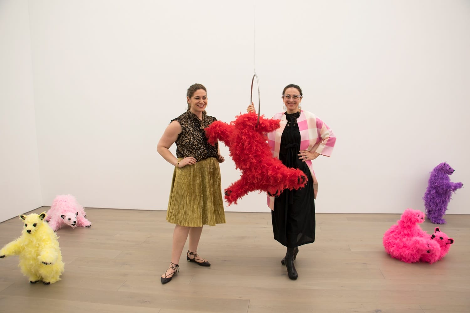 Two people posing with colorful, fluffy animal sculptures in an art gallery.