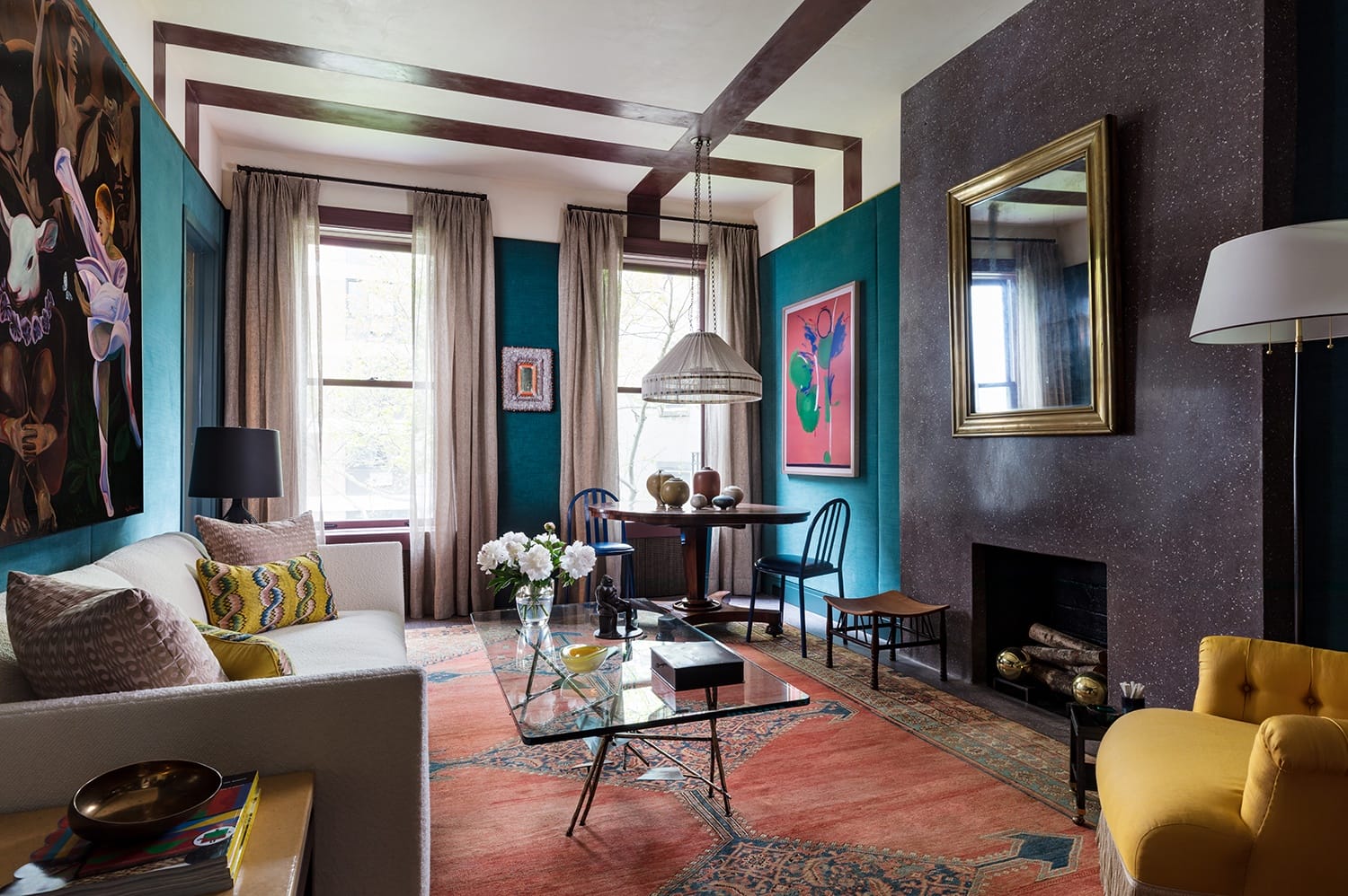 Colorful living room with modern art, glass coffee table, yellow chair, and large windows with curtains letting in natural light.