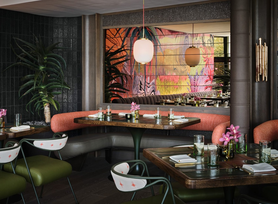 Modern restaurant interior with colorful mural, plush seating, and elegantly set tables with pink flower arrangements.