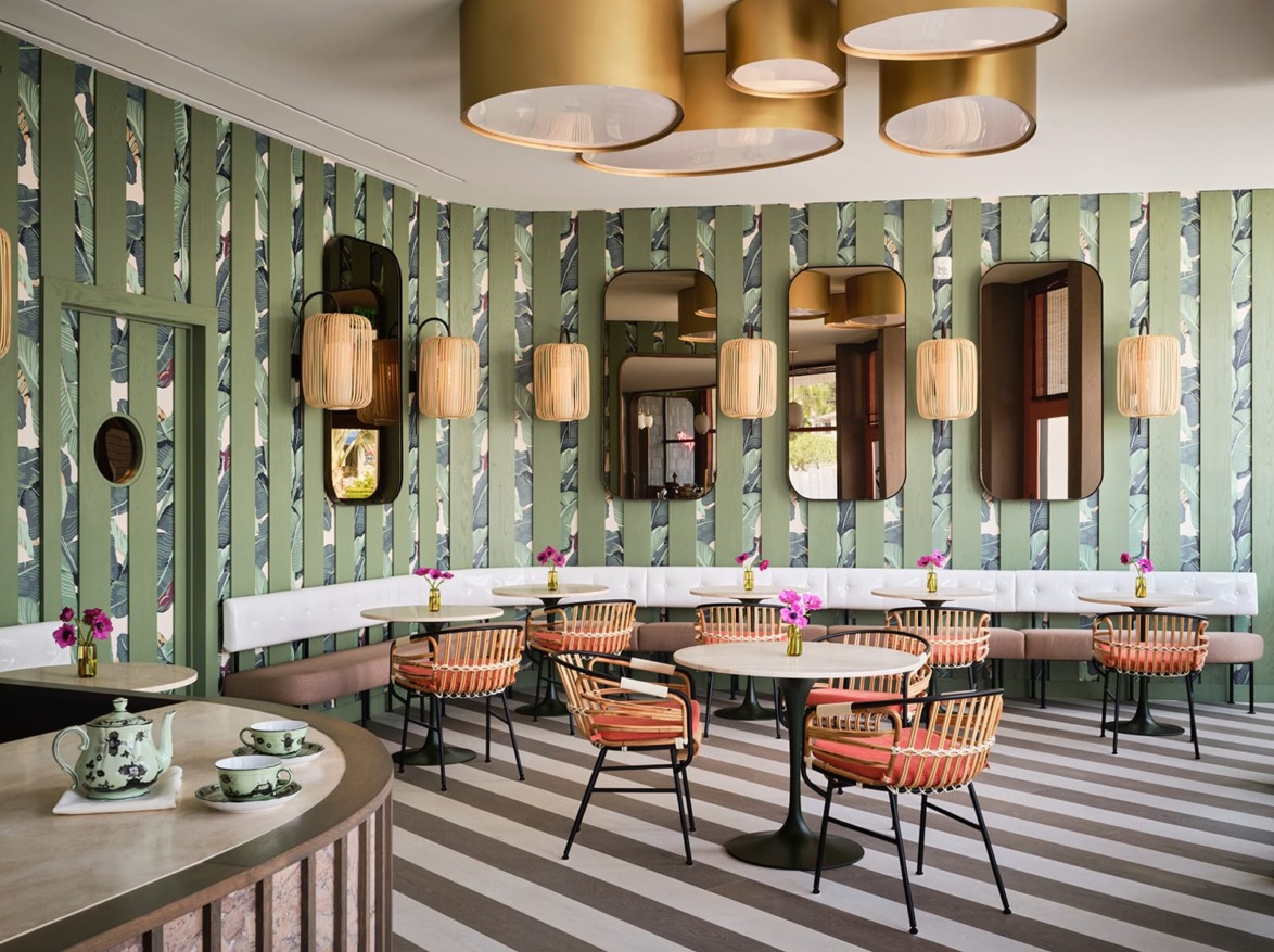 Modern cafe interior with green striped walls, round tables, wicker chairs, and decorative ceiling lights.