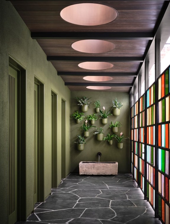 Modern hallway with green walls, hanging plants, stone sink, and colorful stained glass panel windows.