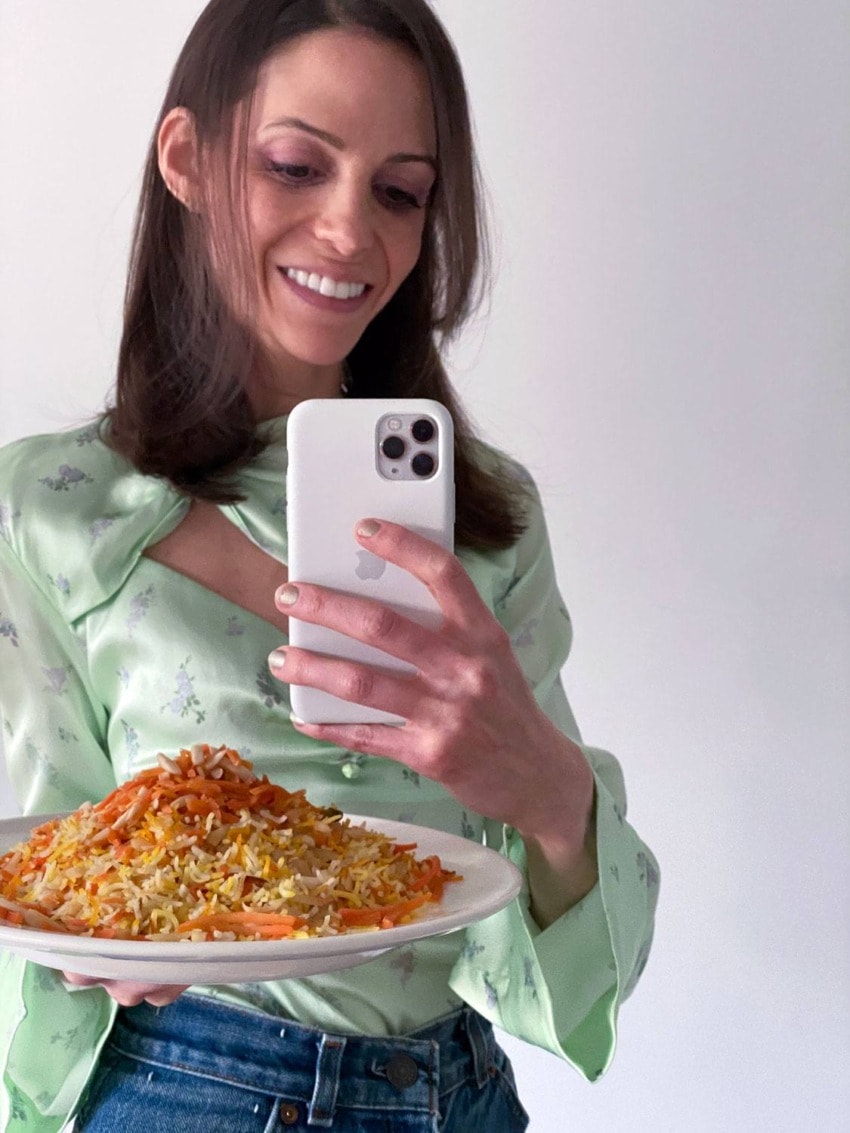 Smiling woman taking a selfie with a plate of colorful rice and vegetables in front of her.