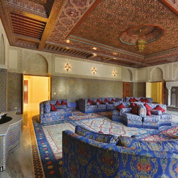 Ornately decorated room with elaborate patterns, blue sofas, and intricate ceiling design in a luxurious setting.