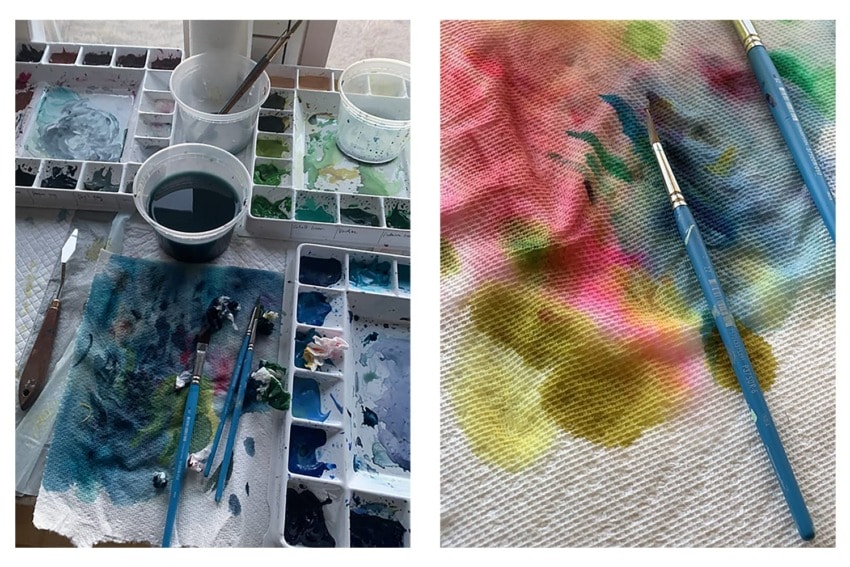 Paintbrushes and a colorful palette on a table with paint splatters on a textured cloth.