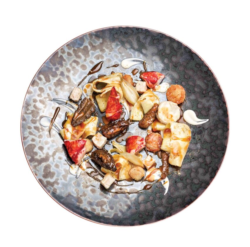 Gourmet dish with assorted vegetables, mushrooms, and sauce artfully arranged on a textured ceramic plate.