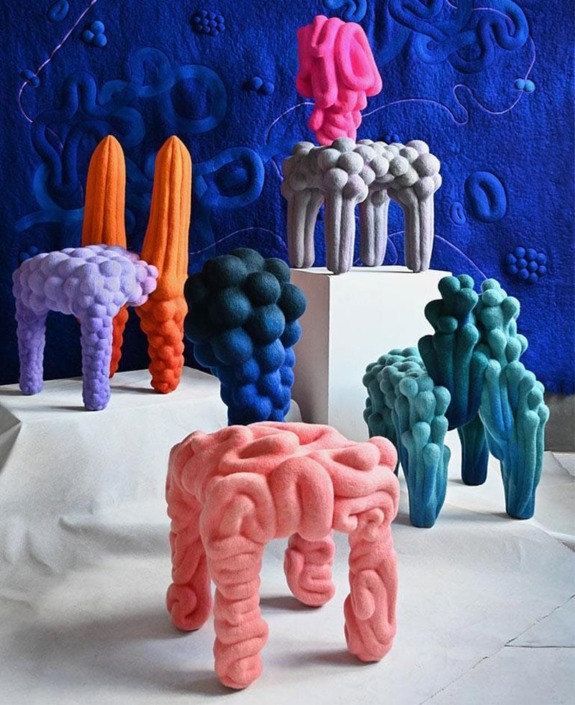 Colorful, abstract 3D sculptures resembling chairs with fabric textures displayed in a vibrant artistic setting.