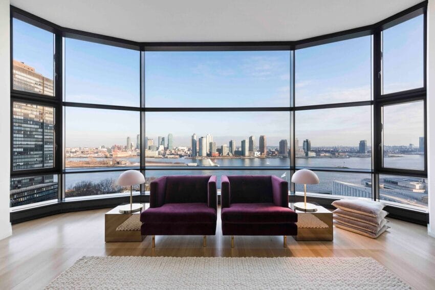 Modern living room with floor-to-ceiling windows offering a panoramic cityscape and river view, featuring purple chairs.