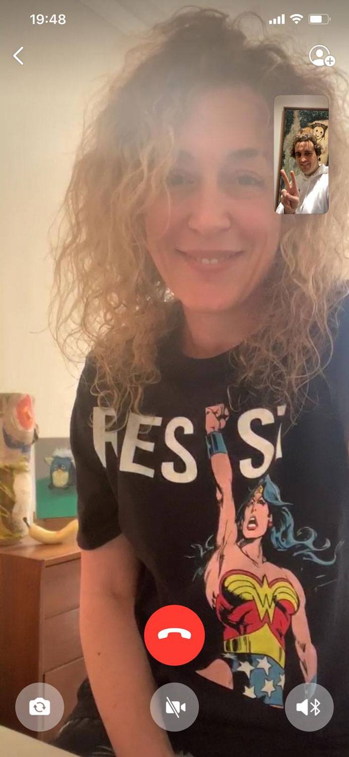 Person with curly hair wearing a Wonder Woman shirt on a video call, small screen shows peace sign gesture