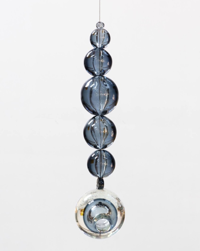 Dangling glass ornament with graduated beads and a large translucent sphere at the bottom against a plain background.