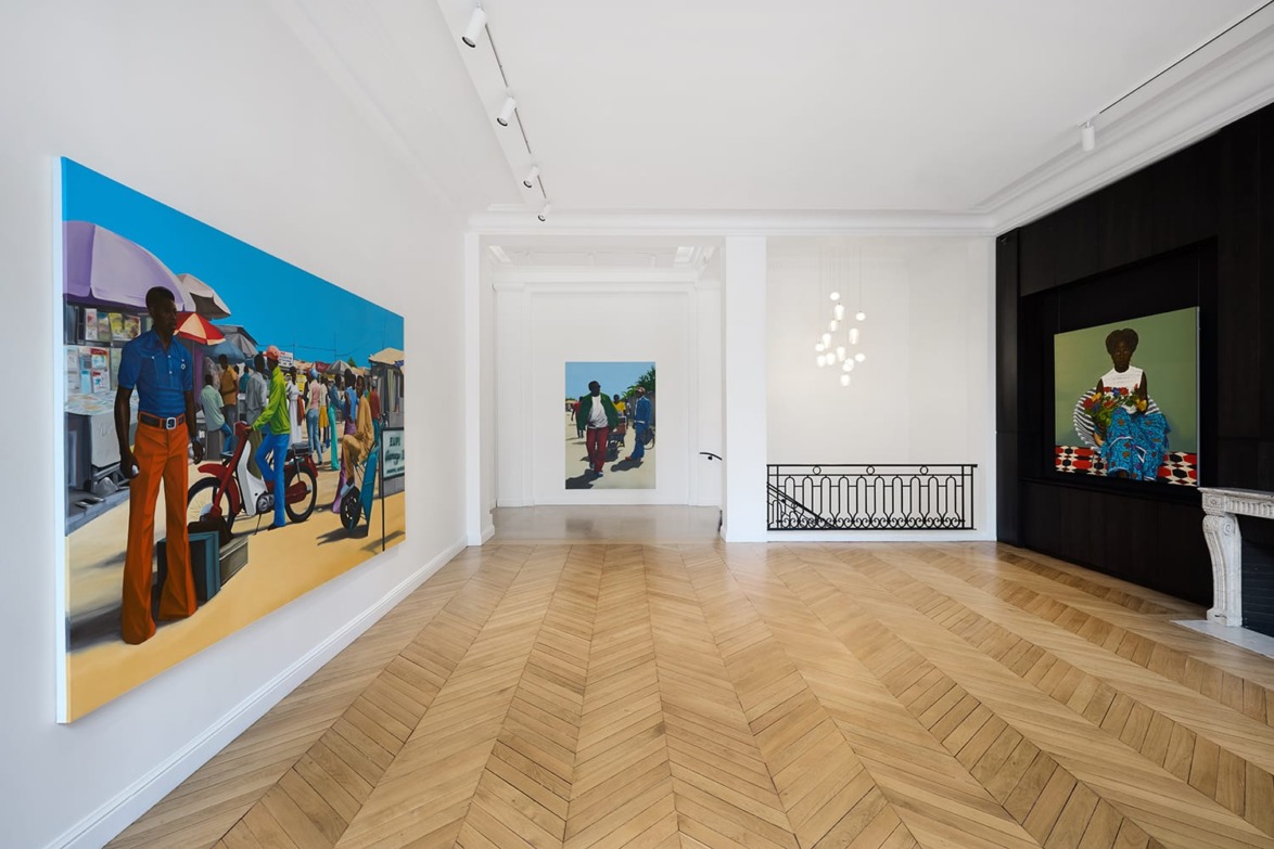 Contemporary art gallery interior showcasing colorful, vibrant paintings on white walls with wooden herringbone flooring.