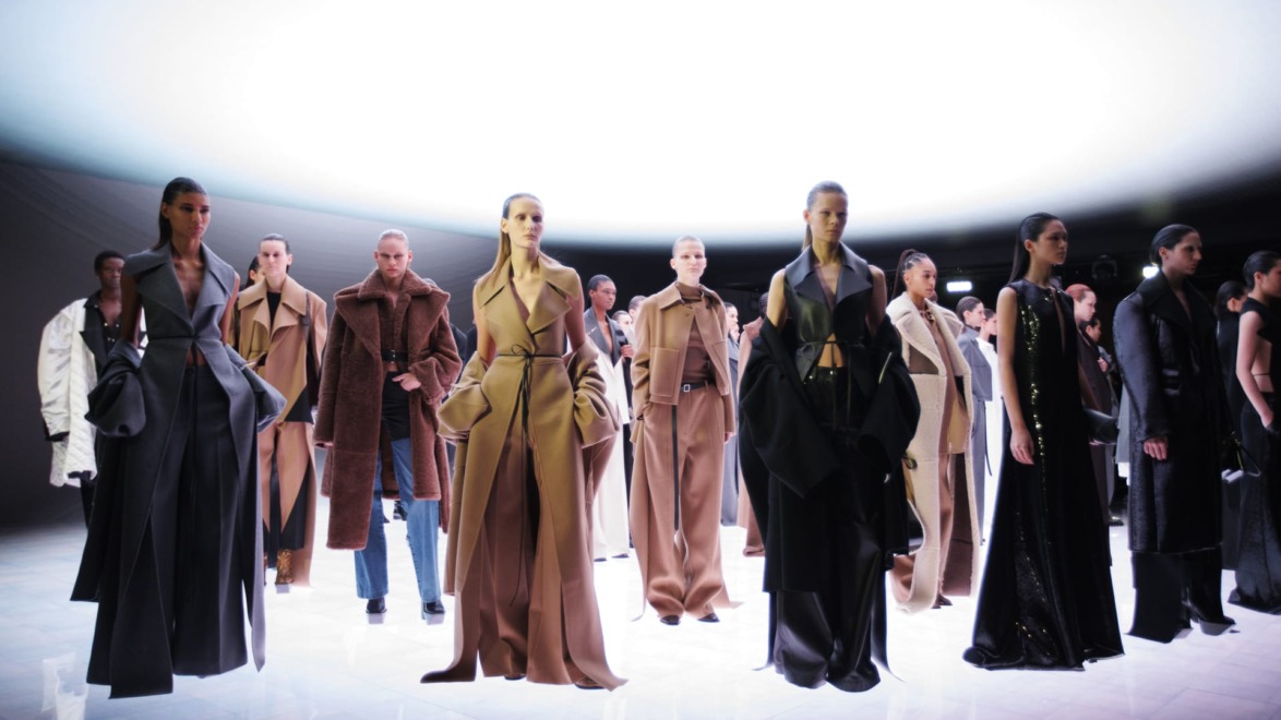 A fashion runway featuring models in elegant, modern outfits under dramatic lighting at a fashion show.