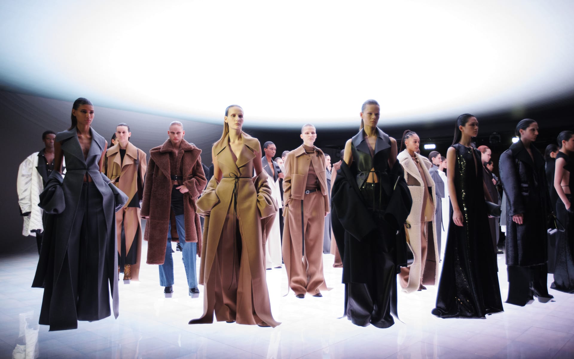 A fashion runway featuring models in elegant, modern outfits under dramatic lighting at a fashion show.