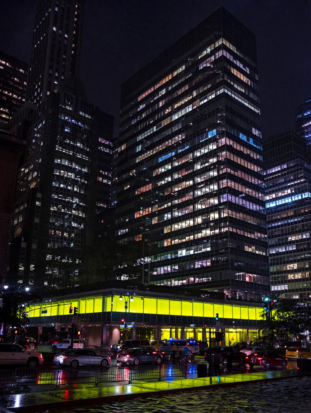 Night view of illuminated office buildings and traffic on wet streets reflecting lights in the city.