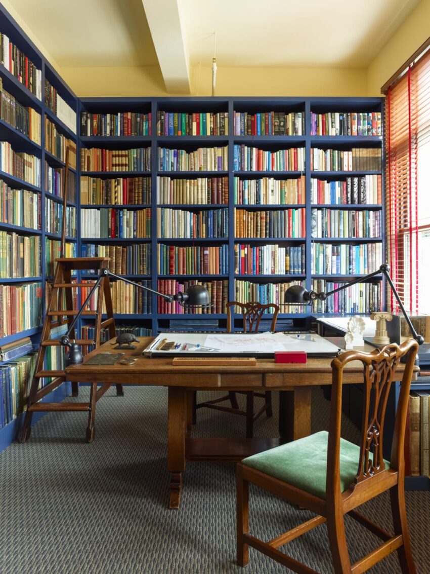 Cozy study room with a wooden desk, vintage chair, and a wall of colorful bookshelves and a ladder for reaching high shelves.