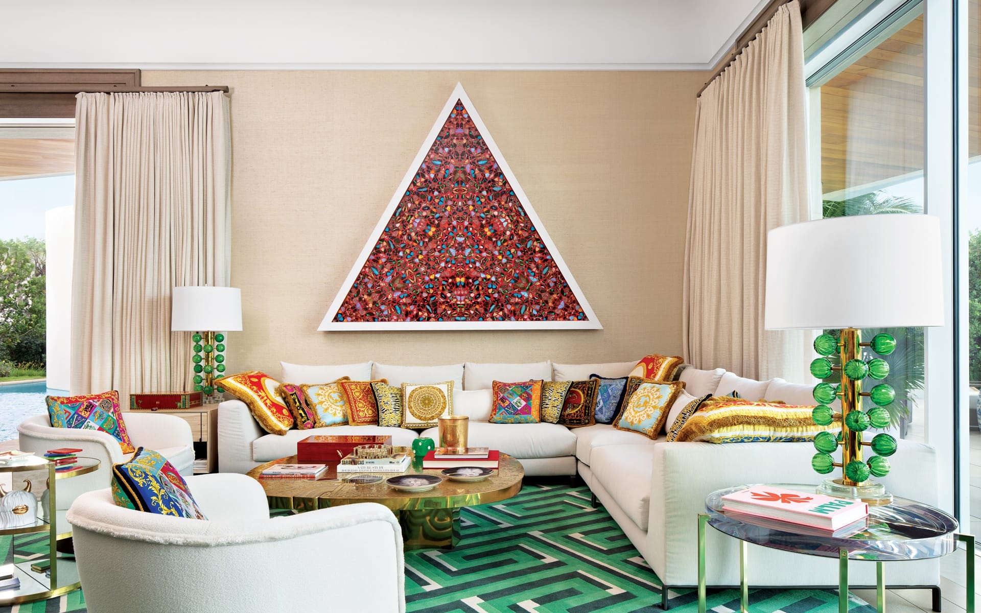 Colorful living room with patterned cushions, triangle art on wall, two white sofas, green lamps, and geometric rug.