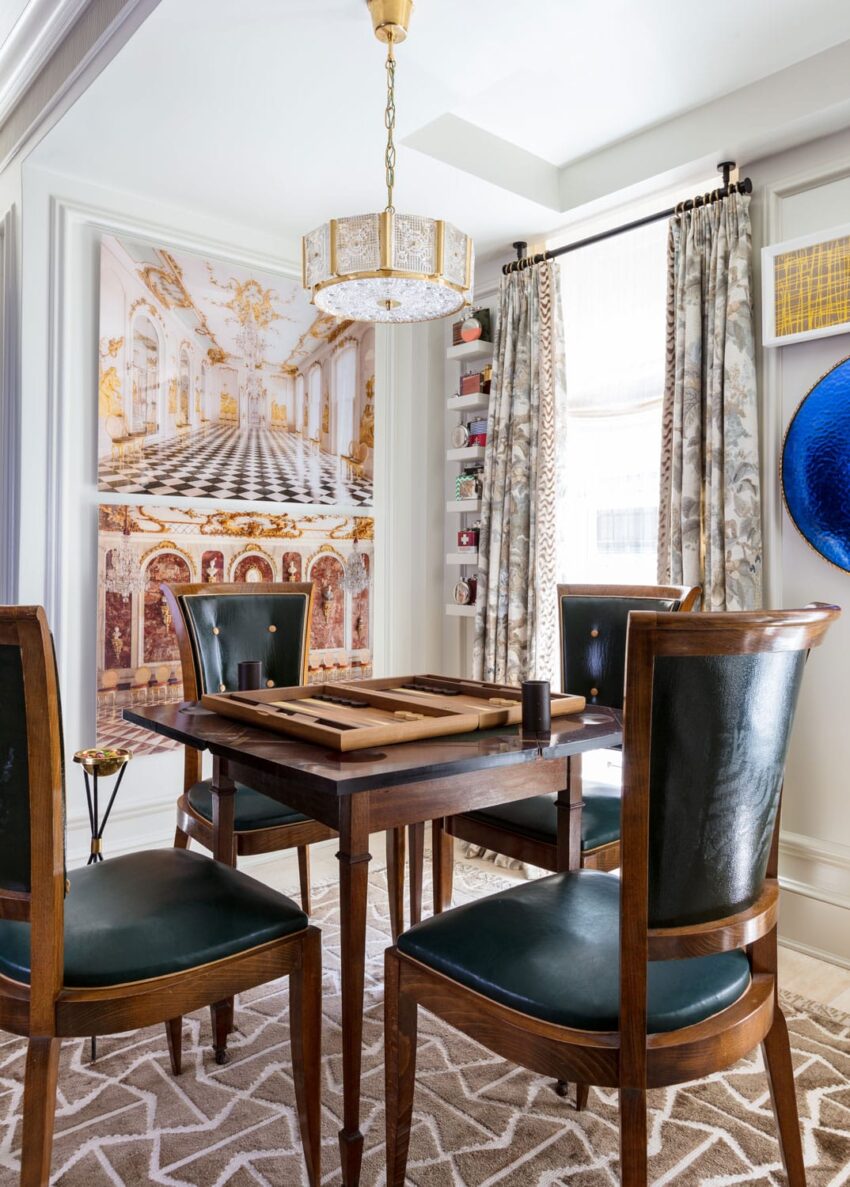 Elegant dining room with wooden table, dark chairs, ornate chandelier, and large wall art featuring a grand interior scene.