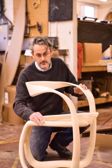 Man in workshop crafting a unique wooden chair, focusing on design details.
