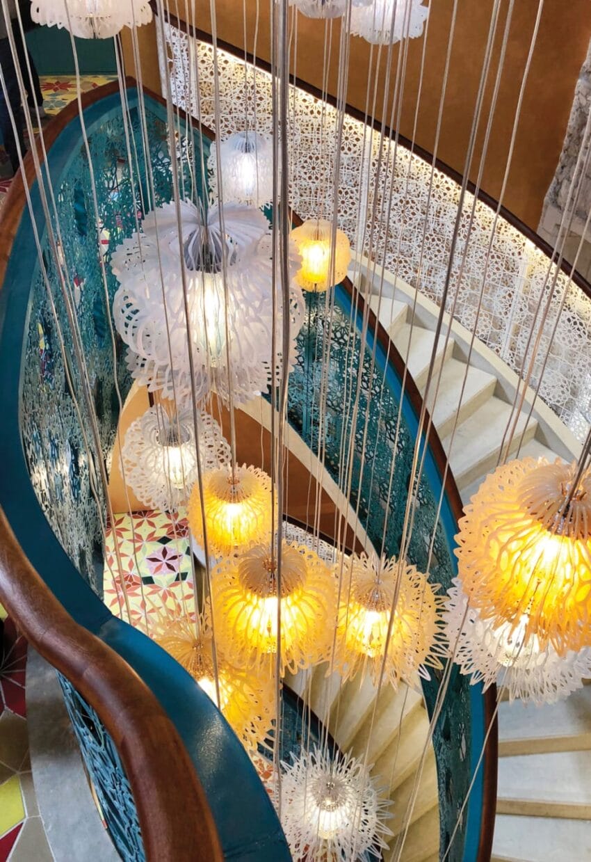 Colorful spiral staircase with intricate railing, hanging decorative lights, and patterned floor tiles.