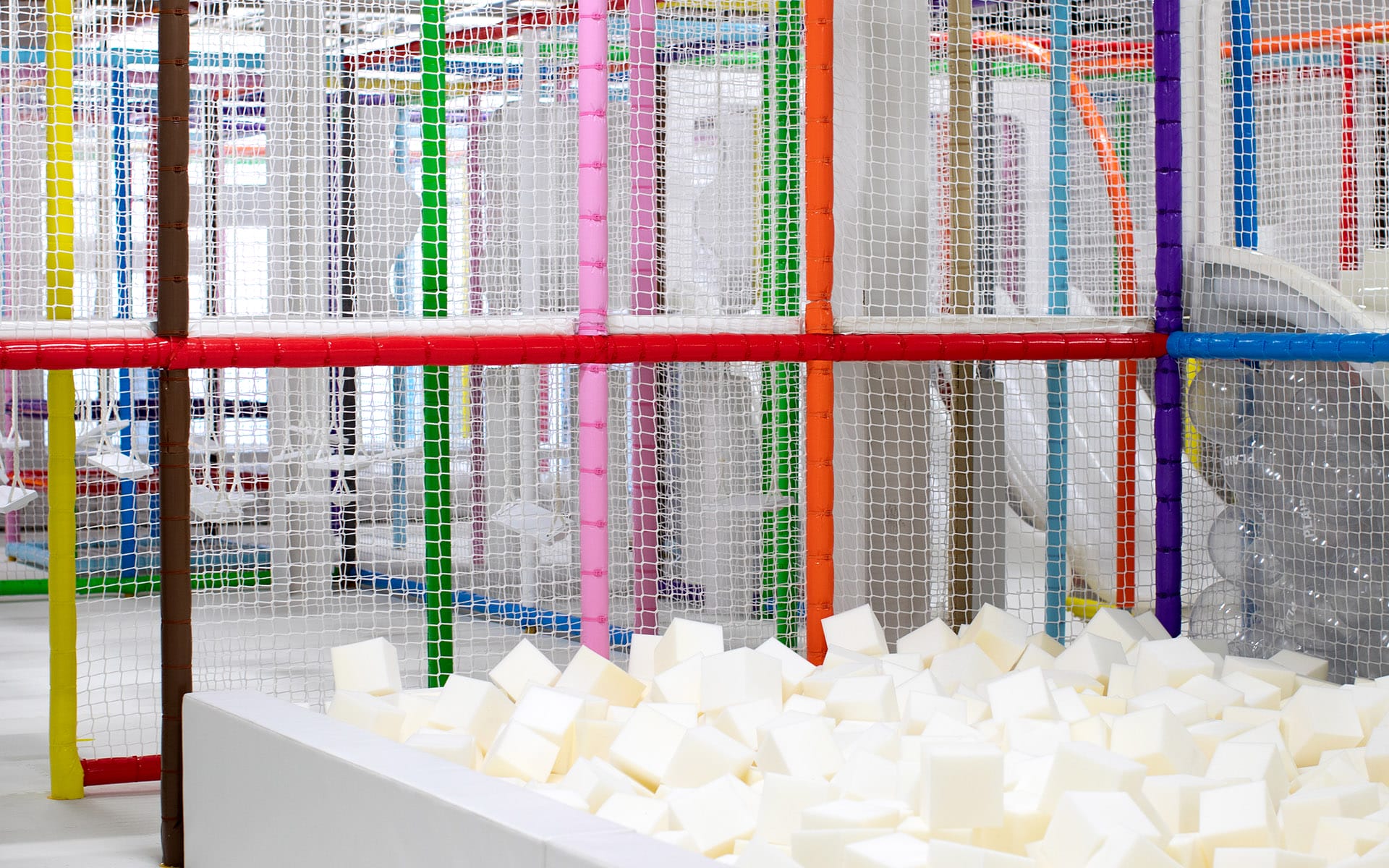Indoor play area with colorful padded poles and a white foam block pit.