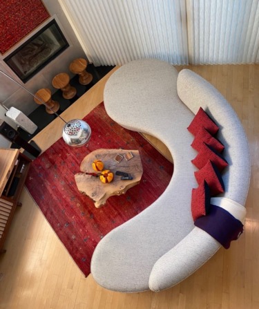 Modern living room with curved sofa, red and wooden accents, and decorative pillows on wooden floor.