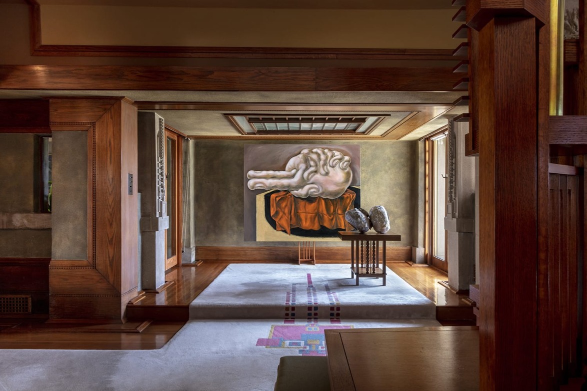 Art-filled room with wooden accents, featuring a surreal painting of a reclining figure and two sculptures on a table.
