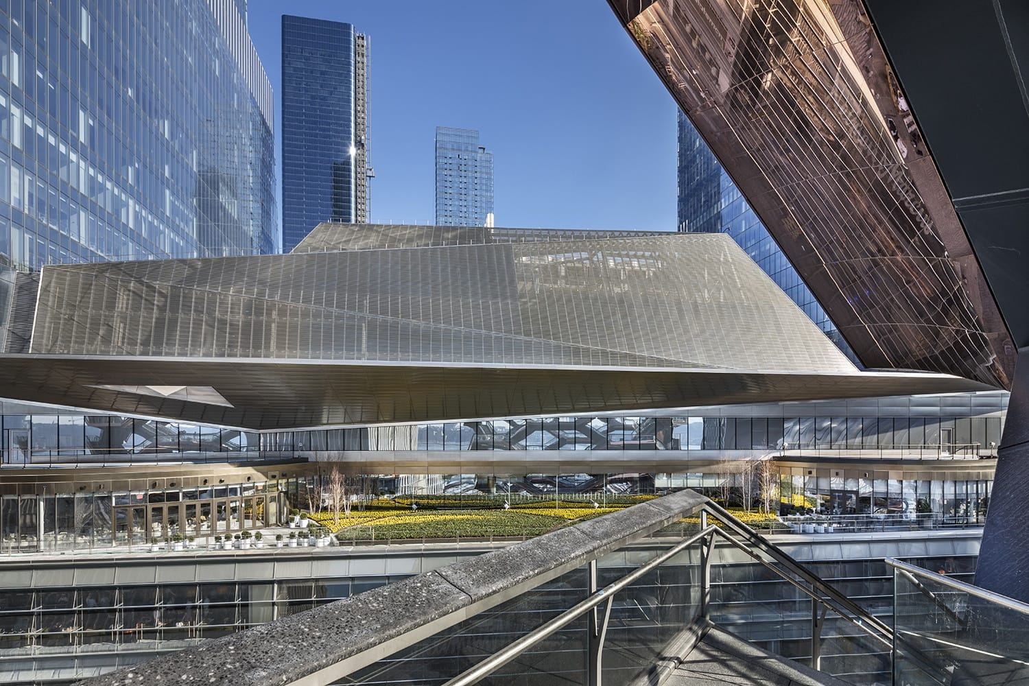 Modern architectural building with geometric shapes, surrounded by tall skyscrapers, under a clear blue sky.