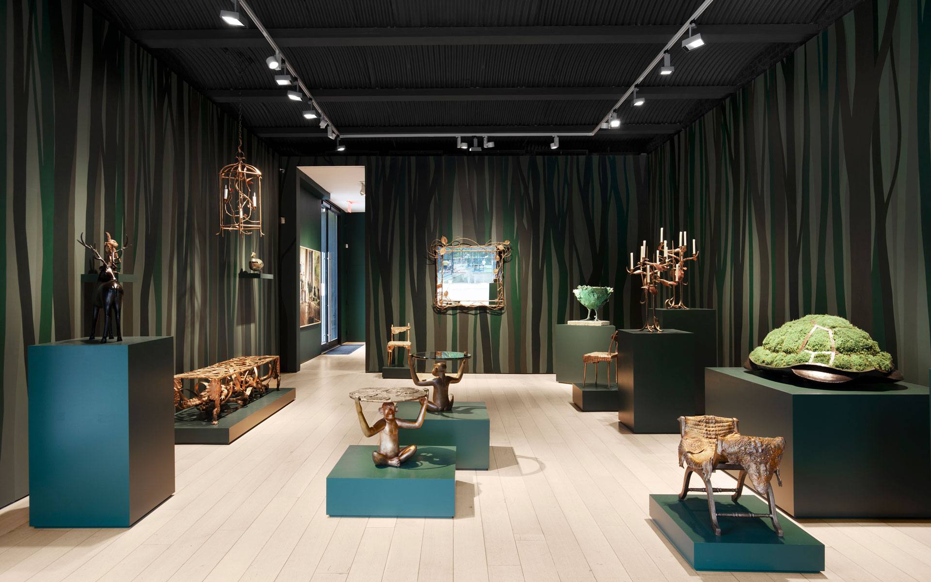 Art gallery interior with sculptures, elegant furniture, and a decorative mirror on forest-themed walls.