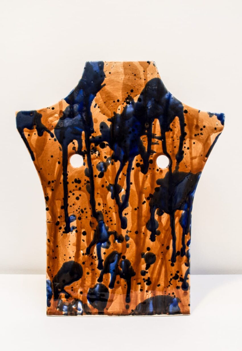 Abstract ceramic sculpture with blue and orange glaze, featuring an irregular shape and two large circular cutouts.