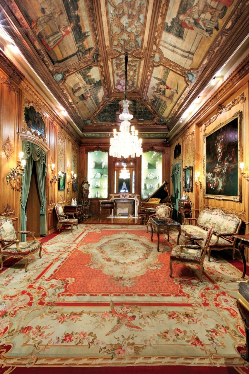 Ornate vintage room with chandelier, antique furniture, painted ceiling, and decorative carpet.