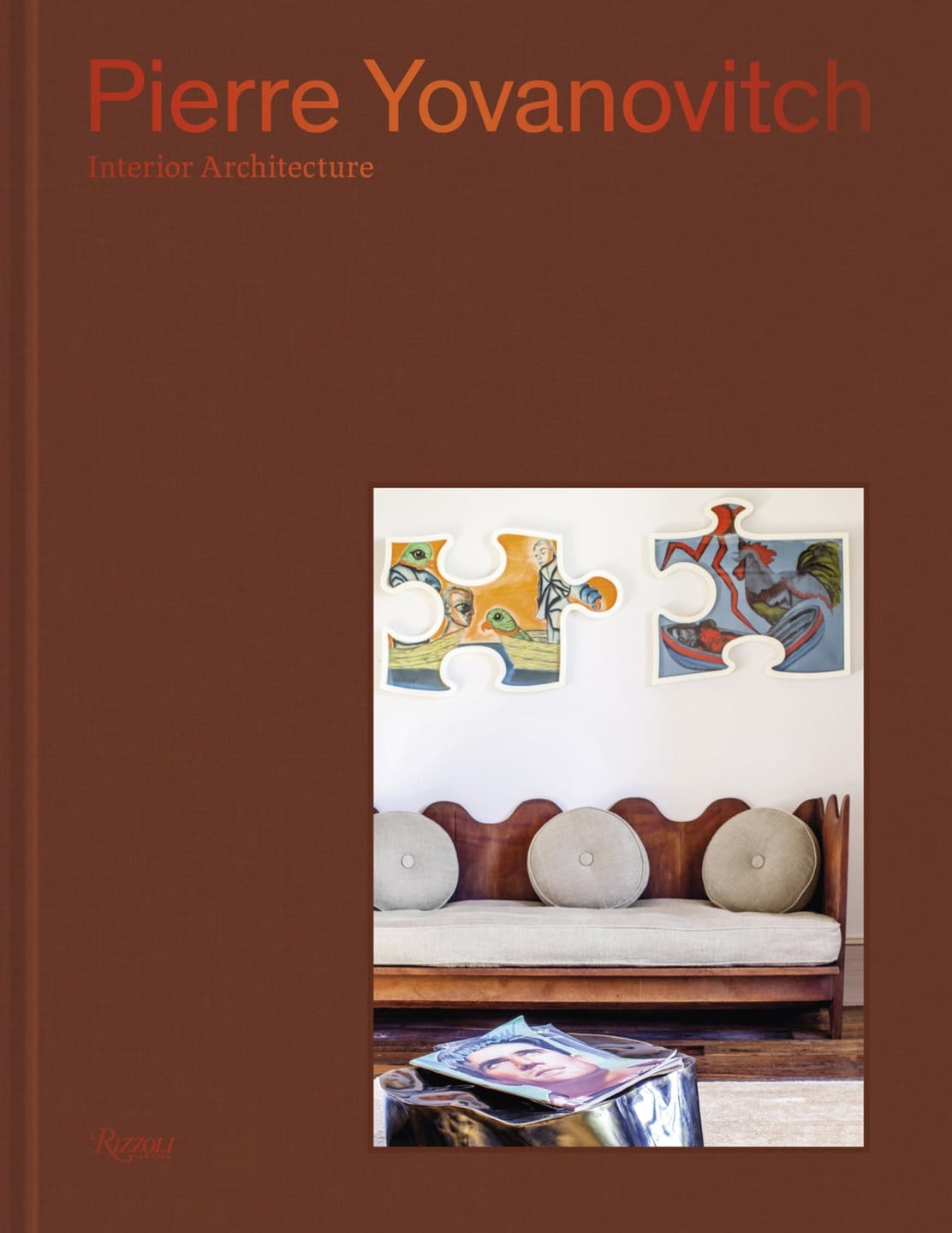 Book cover of "Pierre Yovanovitch: Interior Architecture" featuring a brown background and puzzle piece artwork above a sofa.