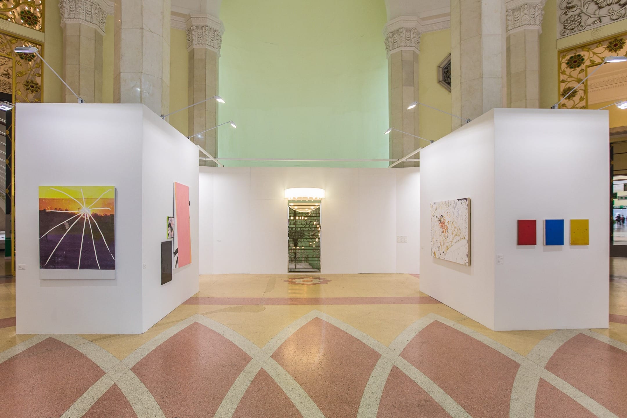 Art gallery with colorful abstract paintings displayed on the walls, bright lighting, and ornate architectural details in the background.