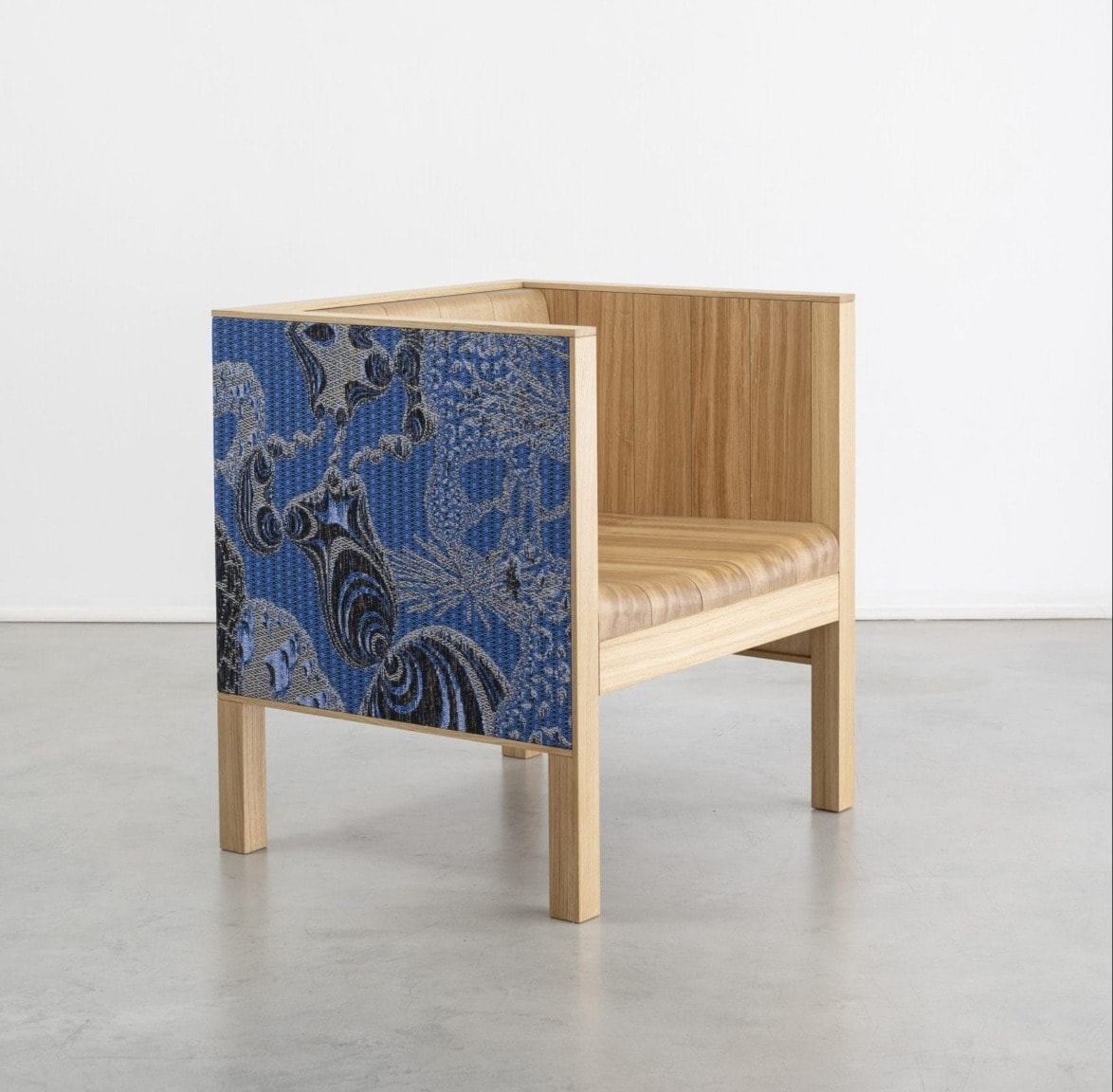 Modern wooden chair with blue patterned fabric side panel, set against a plain white background.