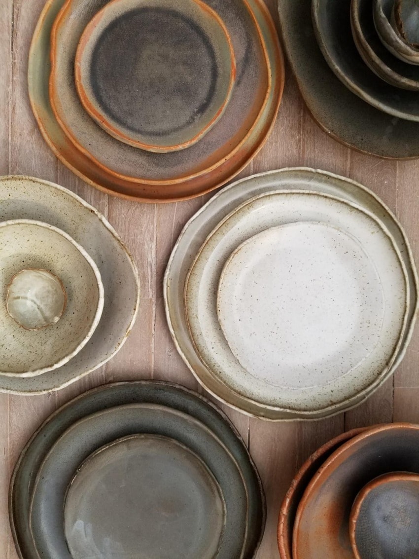 Ceramic plates with earthy tones stacked on a wooden surface, showcasing various sizes and natural textures.