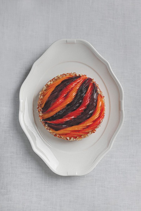 Colorful layered tart on an elegant white plate, featuring vibrant red, orange, and black swirls.